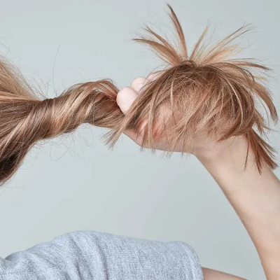Hair Styles Can Damage Your Hair and Potentially Contribute Hair Loss - the back portion of a woman's head - she is facing to the left, twisting her hair into a messy ponytail and pulling with her left hand.