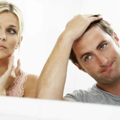 Hair Loss Test Everyone Should Know - a woman and a man looking into a mirror, each with their hand in their hair, to determine the severity of their hair loss.