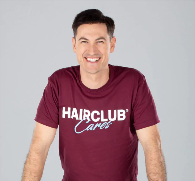 Celebrity Joey Logano - with a full head of hair, wearing a burgundy HairClub Cares t-shirt, and smiling about his HairClub Xtrands+ solution.
