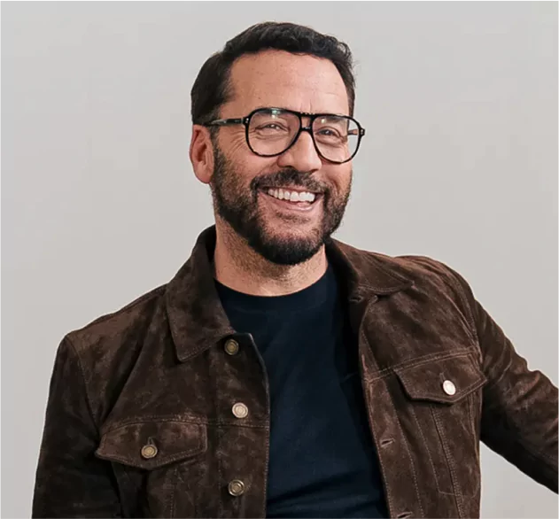 Celebrity Jeremy Piven - has a full head of hair and a big smile - he is wearing a black t-shirt and a light-weight brown jacket.