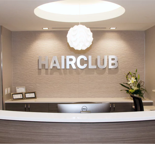 HairClub Franchise Opportunities - the reception desk of a HairClub Center - the HairClub logo in silver is hanging on the wall behind the desk.
