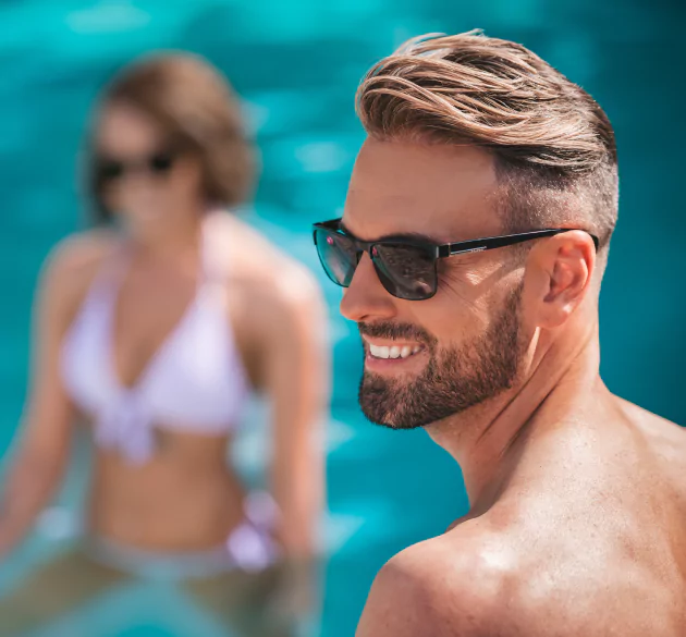 HairClub Hair Assessment Quiz - a guy with good hair, wearing sunglasses at the pool - there is a women out of focus off to the side behind him.