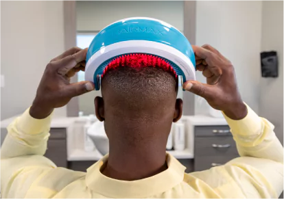 HairClub -Laser Treatment - Stop Hair Loss - the back of a man's head - he is using both hands to put a laser light therapy device on his head.