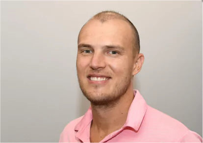 HairClub - RestorInk - Real Hair Appearance - a man in a pink shirt, smiling and posing for a photo to show how RestorInk gives the appearance of real hair.