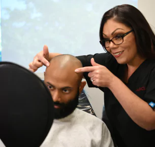 HairClub - Solutions for Hair Loss - a HairClub Hair Loss Specialist uses her pointer fingers to point out a client's hairline while the client looks into a mirror.