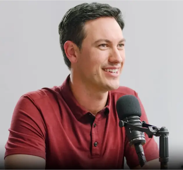 Celebrity Joey Logano - Testimonial - podcasting with a microphone in front of him - he is wearing a burgundy polo shirt and has a full head of hair.