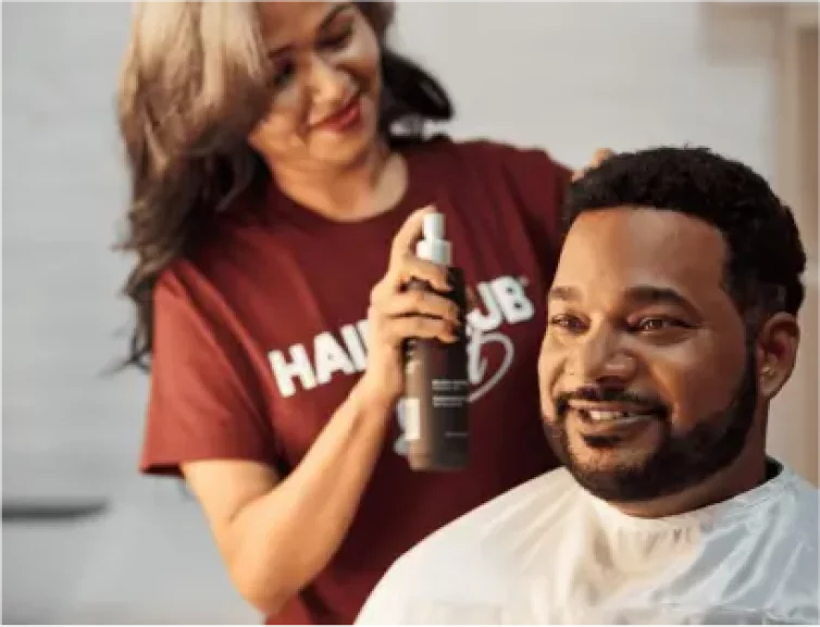 Results - a man with a nice full head of hair sits in a HairClub Center Salon chair as a HairClub Hair Loss Specialist puts product in his hair.